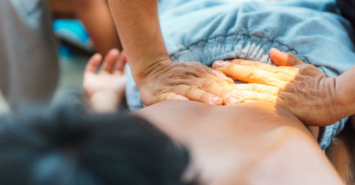 Hands performing a therapeutic massage on a person's back in a serene setting.